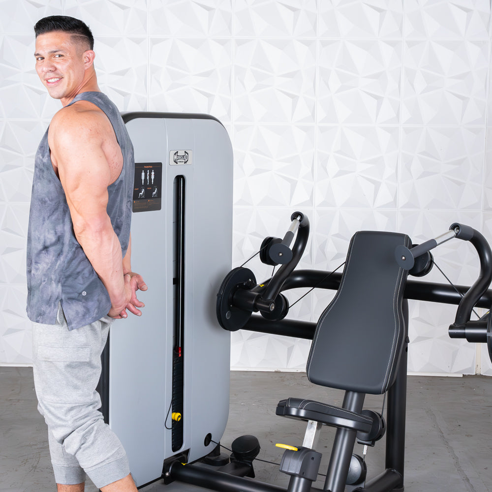 Man standing beside a triceps extension machine in a gym.