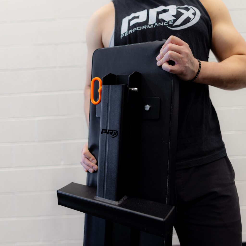 Athlete in a sleeveless shirt holding a gym machine with an orange handle.