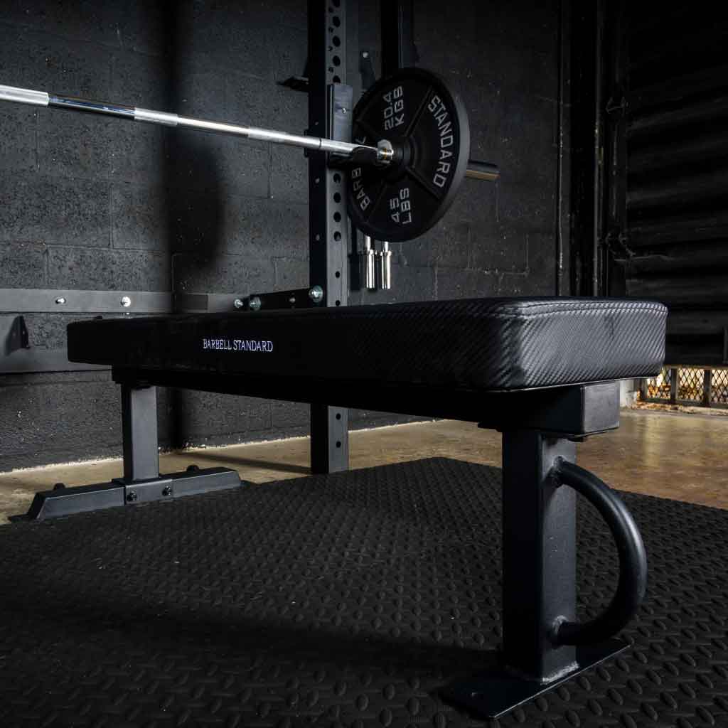 Weight bench with barbell and plates in a dark gym.