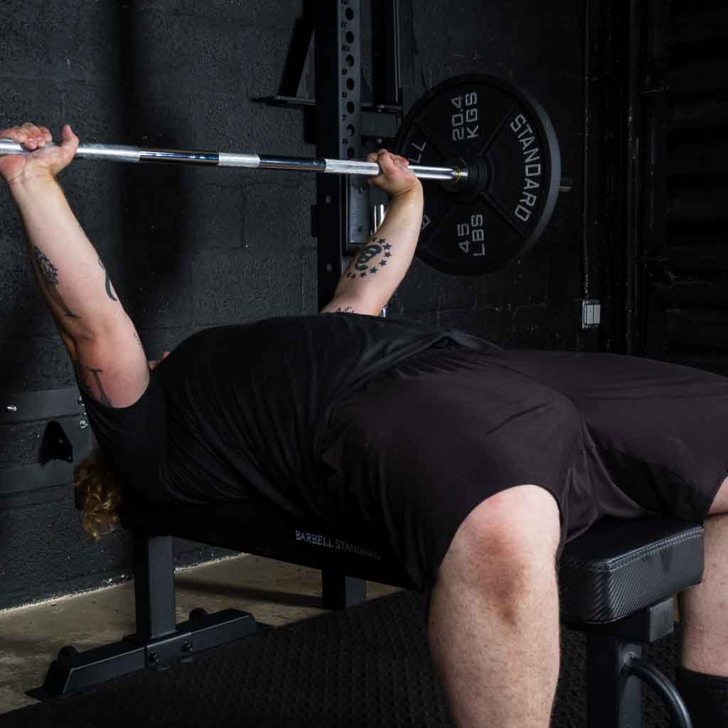 Person bench-pressing a barbell with weighted plates in a gym.