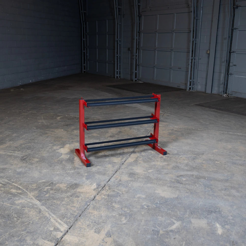 A red and black weight storage rack with three horizontal bars, placed in an empty warehouse with concrete flooring and gray walls.