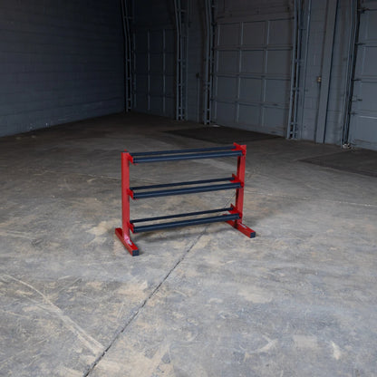 A red and black weight storage rack with three horizontal bars, placed in an empty warehouse with concrete flooring and gray walls.