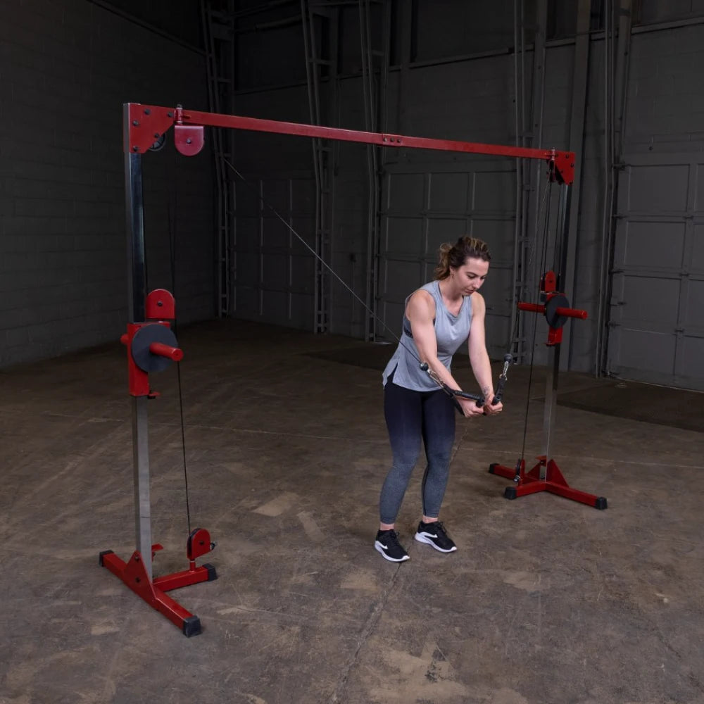 A woman in a gray tank top and black leggings performs a cable exercise using a dual cable machine in a gym setting.