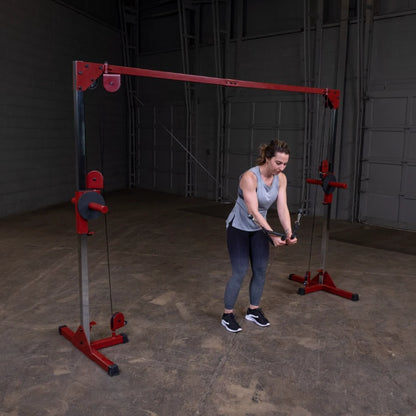 A woman in a gray tank top and black leggings performs a cable exercise using a dual cable machine in a gym setting.