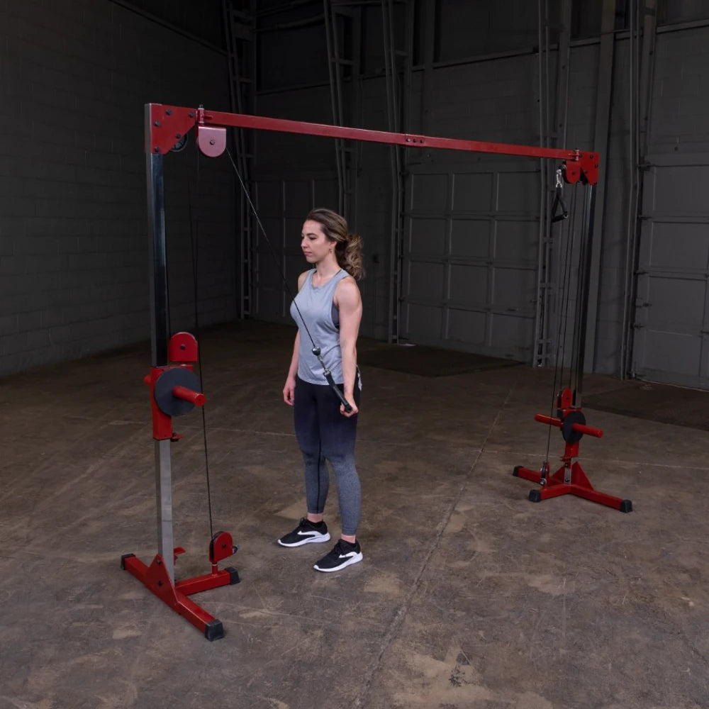 A woman in athletic wear stands in front of a cable machine in a gym, preparing to perform an exercise.