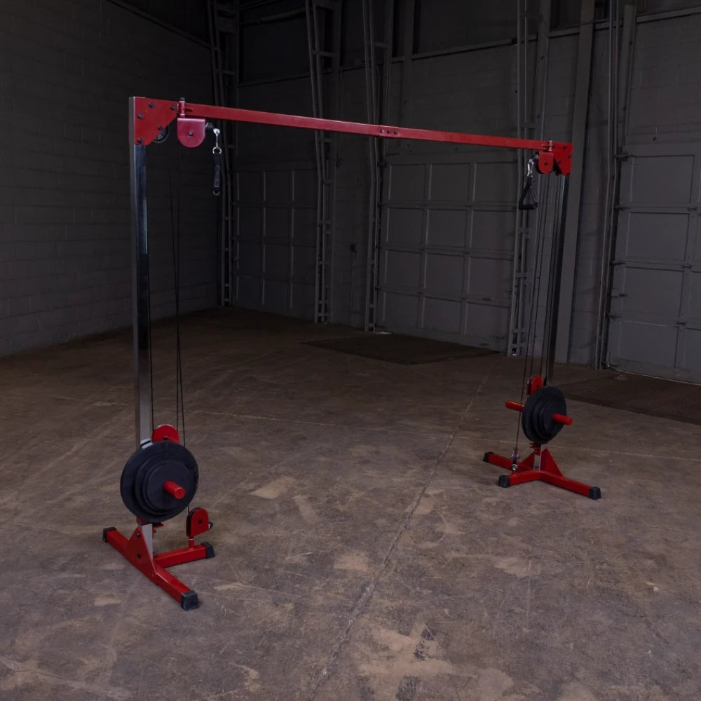 A gym cable machine with a red frame and weights on both sides, set in an empty industrial space with a concrete floor and gray walls.