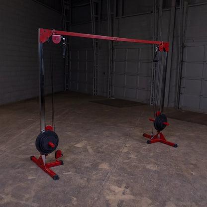 A gym cable machine with a red frame and weights on both sides, set in an empty industrial space with a concrete floor and gray walls.
