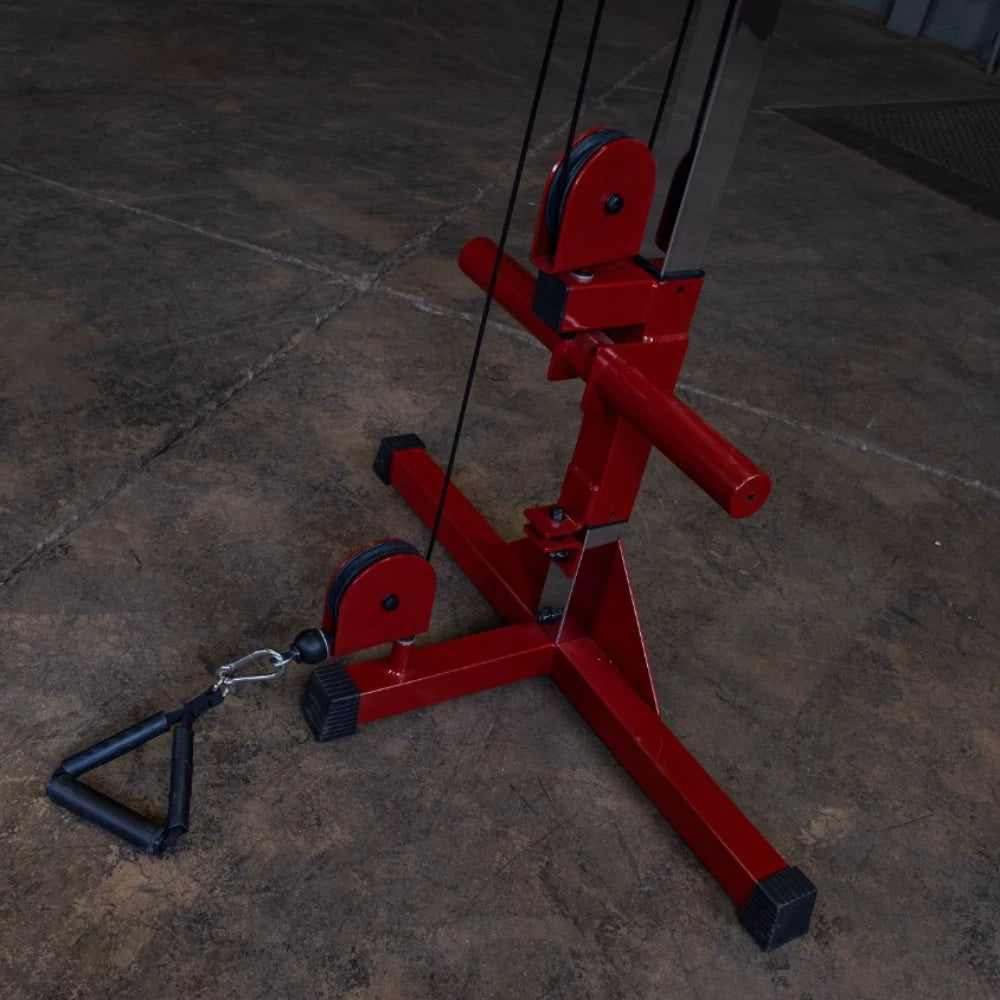 A close-up view of a red cable machine with pulleys and a handle attachment on a concrete floor, designed for strength training exercises.