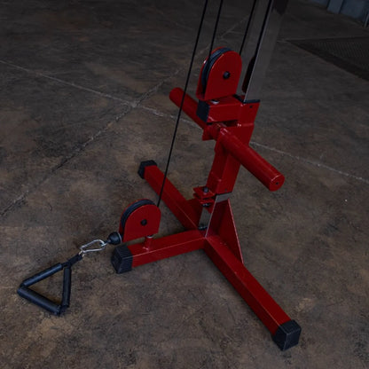 A close-up view of a red cable machine with pulleys and a handle attachment on a concrete floor, designed for strength training exercises.
