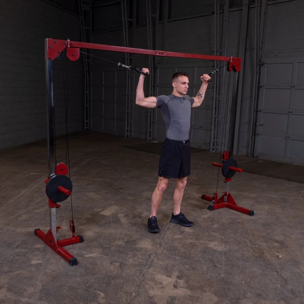 **ALT tag**: A man performing an overhead exercise using a cable machine in a gym setting, wearing a fitted gray shirt and black shorts.