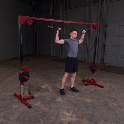 **ALT tag**: A man performing an overhead exercise using a cable machine in a gym setting, wearing a fitted gray shirt and black shorts.