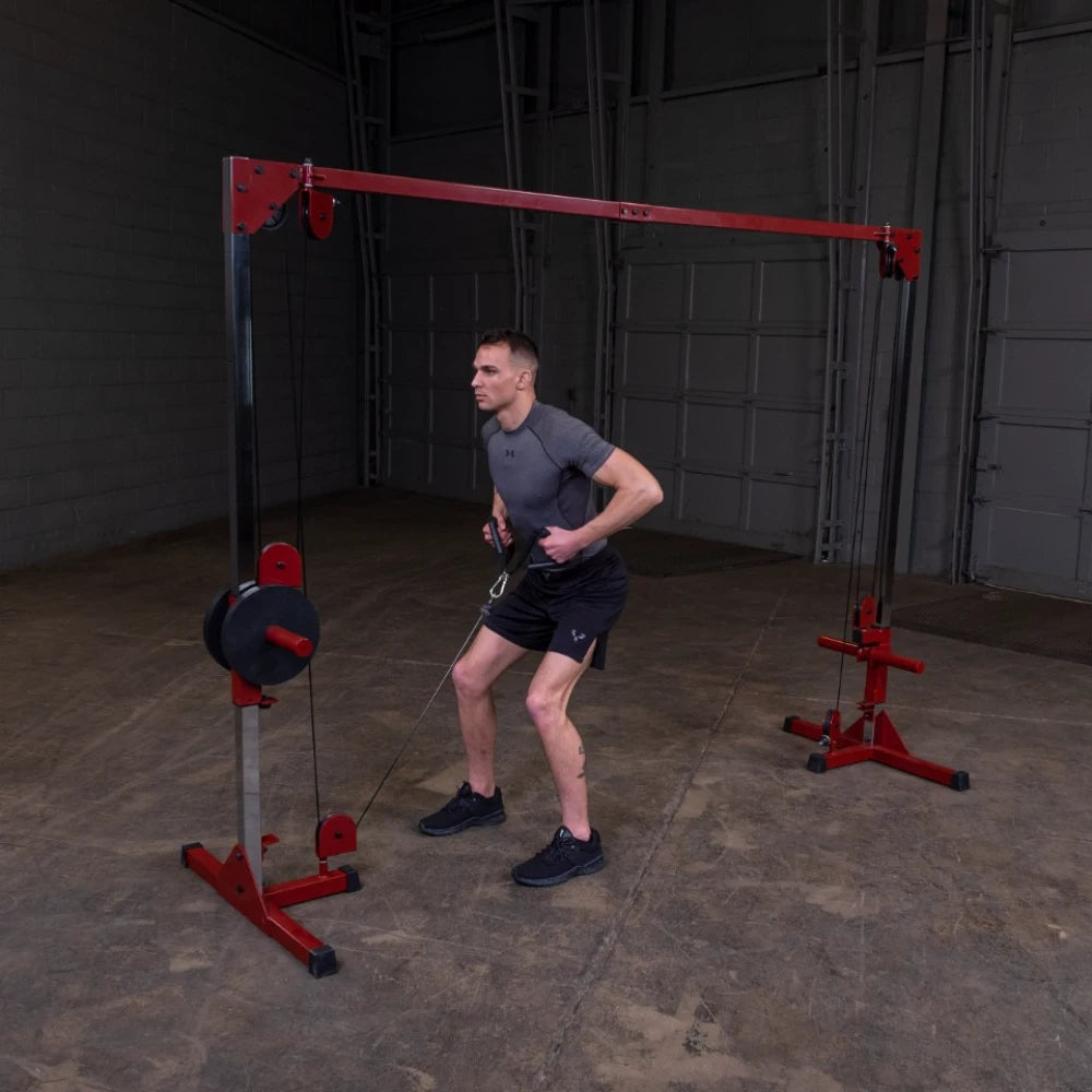 A man performing a cable exercise in a gym, using a cable machine with a red and black design, standing on a concrete floor.