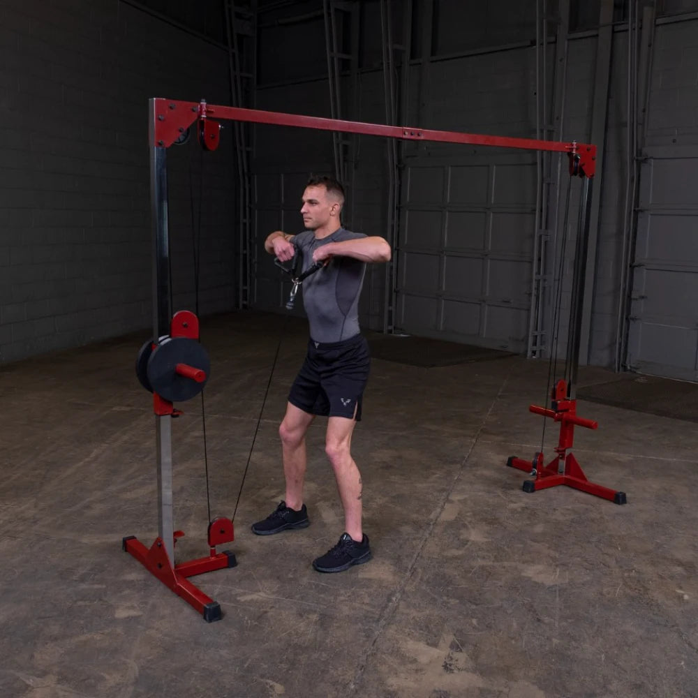 A man in a fitted gray shirt and black shorts performs a cable exercise using a weight machine in a gym setting, focusing on his upper body strength.