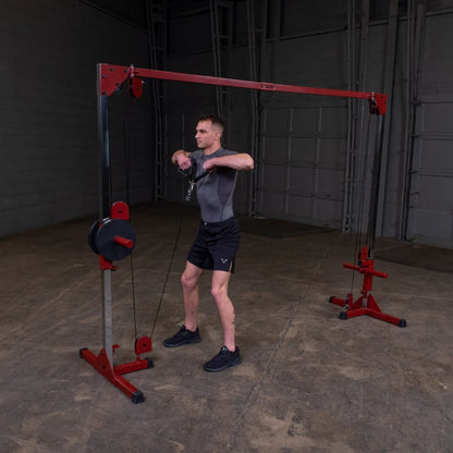 A man in a fitted gray shirt and black shorts performs a cable exercise using a weight machine in a gym setting, focusing on his upper body strength.