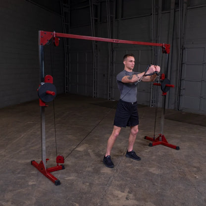 A person standing in a gym setting using a cable machine for exercise, pulling the handles towards themselves while wearing a fitted gray shirt and black shorts.
