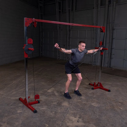 A young man performing an exercise using a cable machine in a gym setting. He is in a squat position, pulling the cables with both hands, showcasing strength training. The gym has a simple, industrial background with gray walls and a concrete floor.