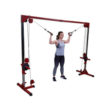 A woman performing an exercise using a cable machine, holding the handles with both hands, while wearing a gray tank top and black leggings.
