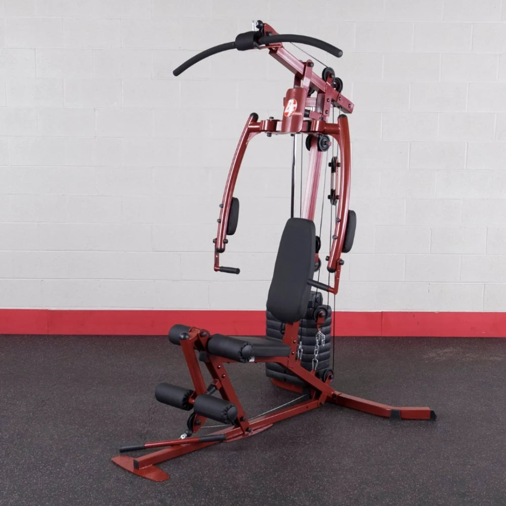 A multi-functional home gym equipment in a red and black color scheme, featuring a pull-up bar, adjustable seat, and various pulleys for strength training, set against a plain wall with a red base.