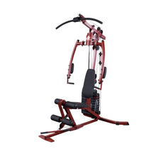 A red and black multi-gym exercise machine designed for strength training, featuring a padded seat, adjustable pulleys, and various attachments for different workouts.