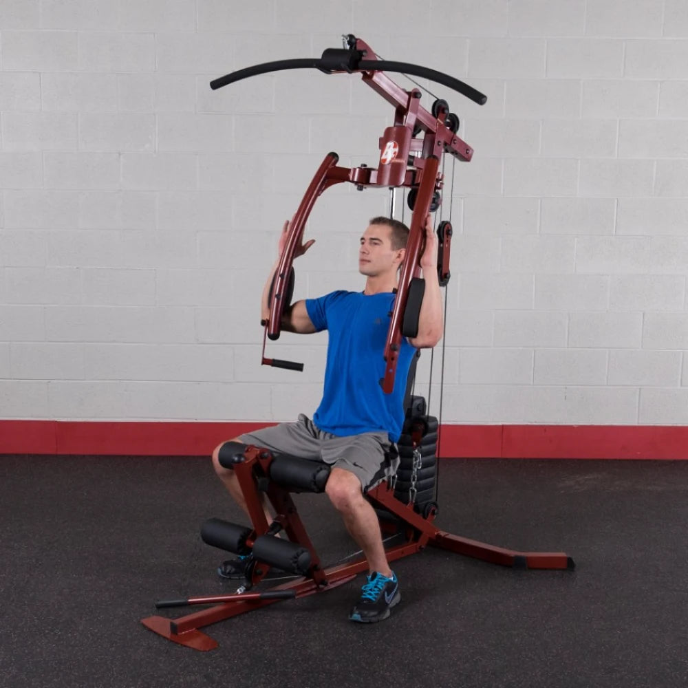 A person performing an upper body exercise on a multi-gym machine, wearing a blue shirt and gray shorts, with a focus on strength training in a gym setting.