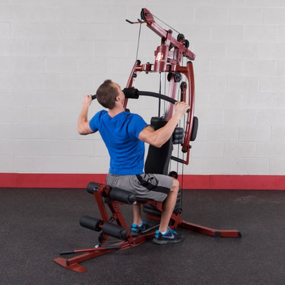 A man in a blue shirt and gray shorts performing a lat pulldown exercise on a gym machine, focusing on upper body strength training.