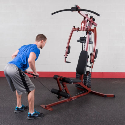 A man in a blue shirt and gray shorts performs an exercise using a multi-station gym machine in a fitness facility.