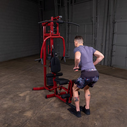 A person performing an exercise on a red gym machine in an indoor training space, wearing a gray shirt and colorful shorts, showcasing a focus on fitness and strength training.