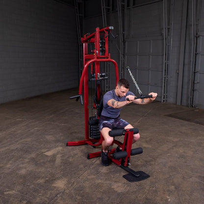 A man exercising on a red multi-gym machine in a spacious gym setting, focusing on his workout with a determined expression.