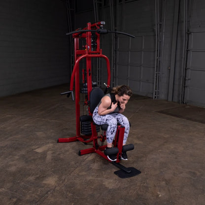 A woman in athletic wear performing an exercise on a red multi-gym machine in a spacious indoor gym setting.