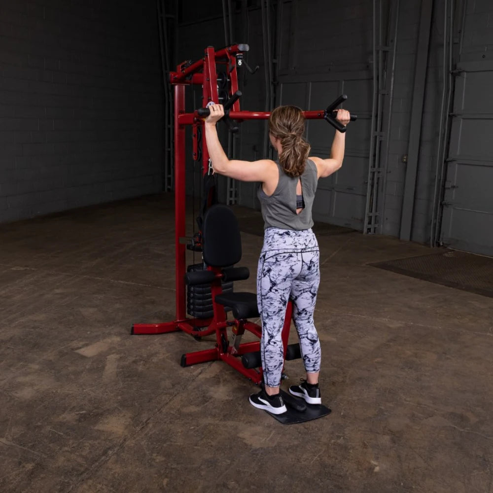 A woman performing an exercise on a weight machine in a gym, wearing a gray tank top and patterned leggings, with her back facing the camera.