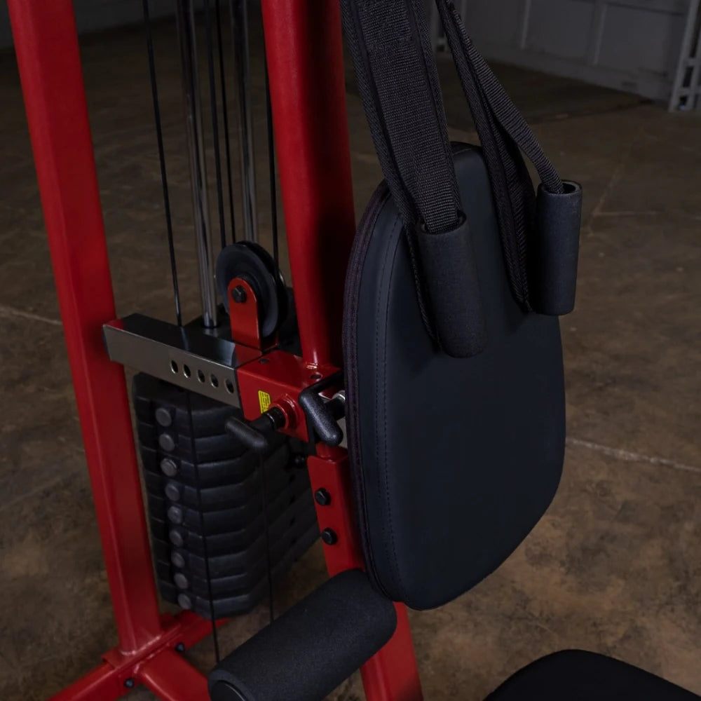 Close-up of a weight machine showing the padded seat and adjustable straps, with a stack of weights in the background, on a gym floor.