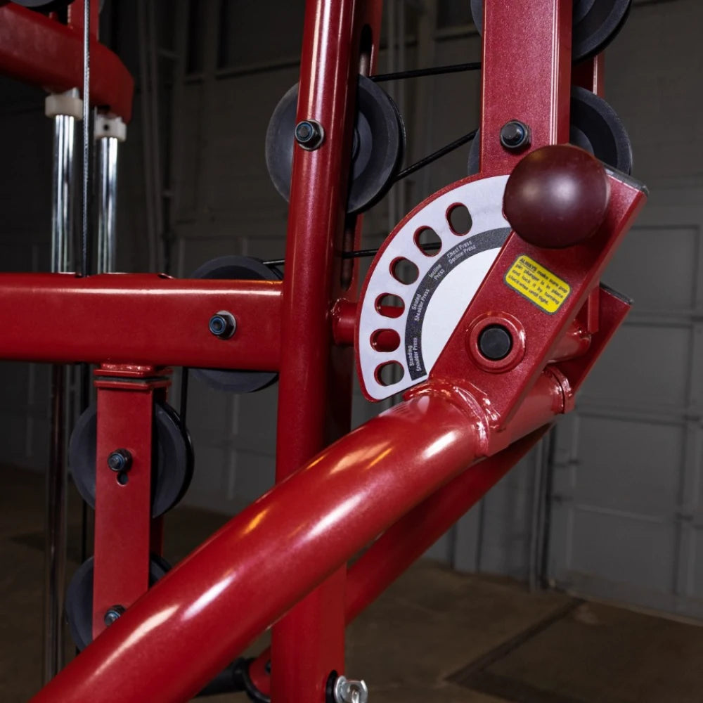 Close-up of a red gym machine showing the weight adjustment mechanism with a dial and several weight plates, set against a blurred background of a gym environment.