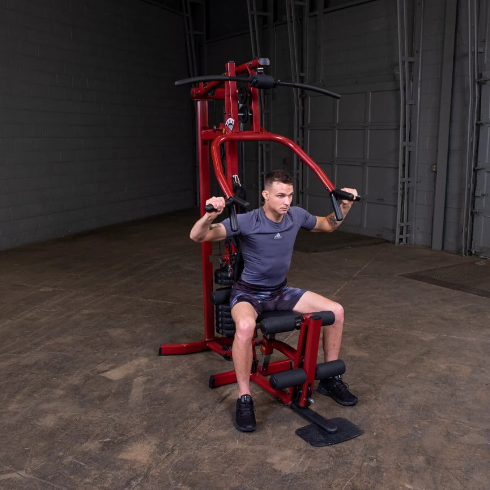 A person exercising on a red multi-gym machine, performing a seated workout in a spacious indoor gym environment.