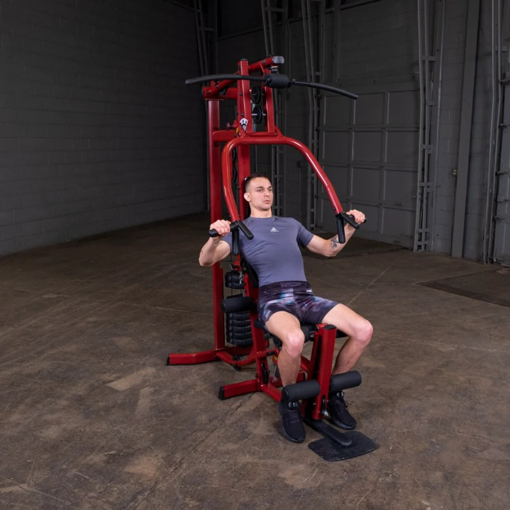 A man exercising on a red multi-gym machine in a spacious indoor setting, demonstrating strength training with focused posture.