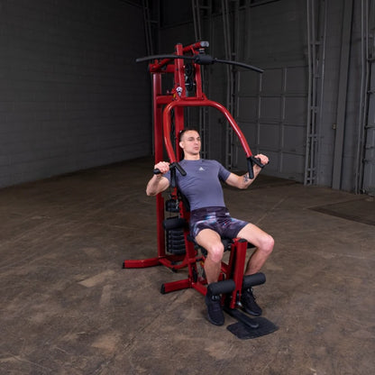 A man exercising on a red multi-gym machine in a spacious indoor setting, demonstrating strength training with focused posture.