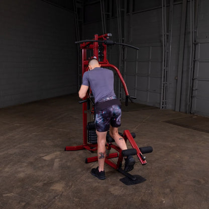 A person wearing a gray shirt and patterned shorts using a red exercise machine in a spacious gym setting.