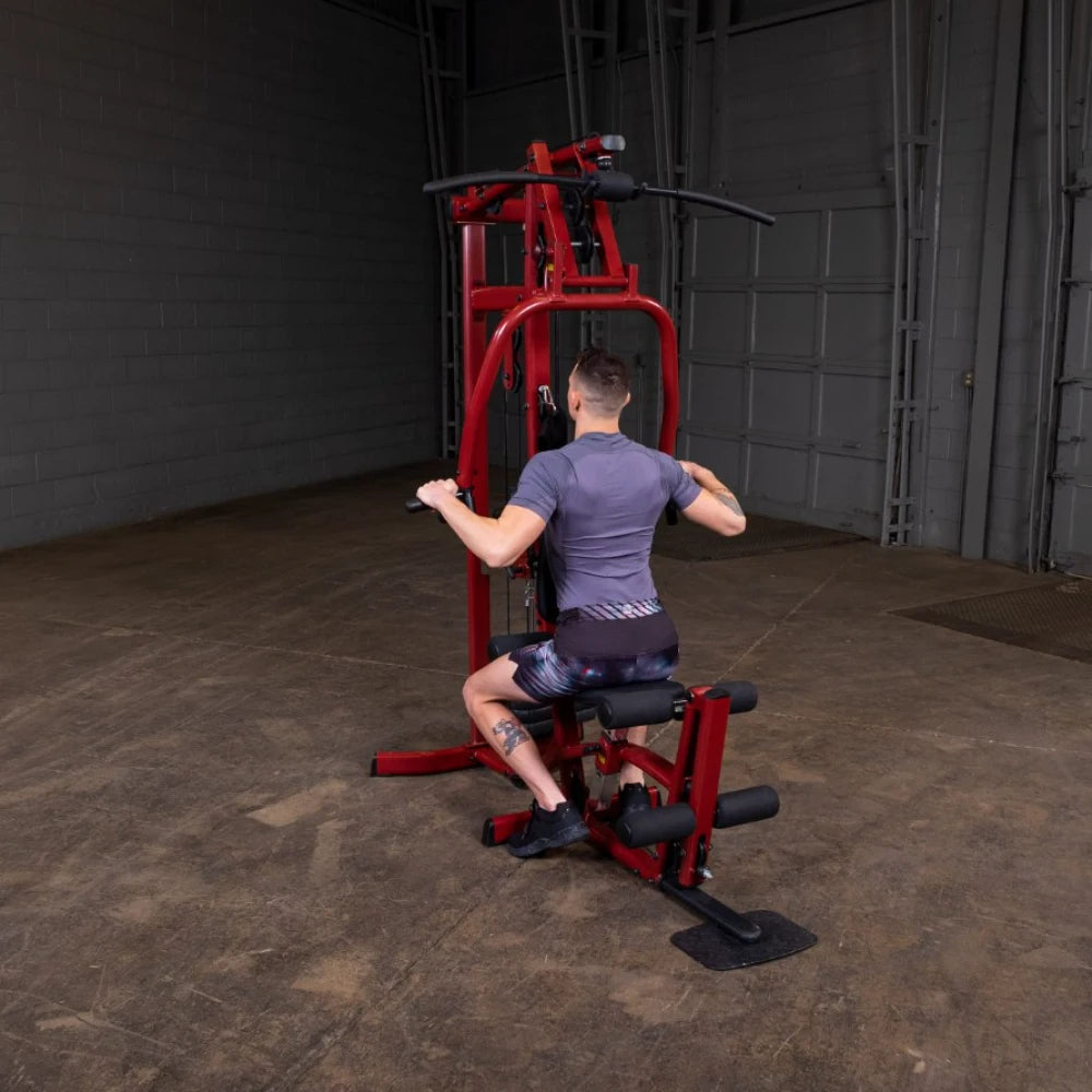 A person performing an exercise on a red gym machine, seated with hands gripping the handles, in an industrial-style gym environment.