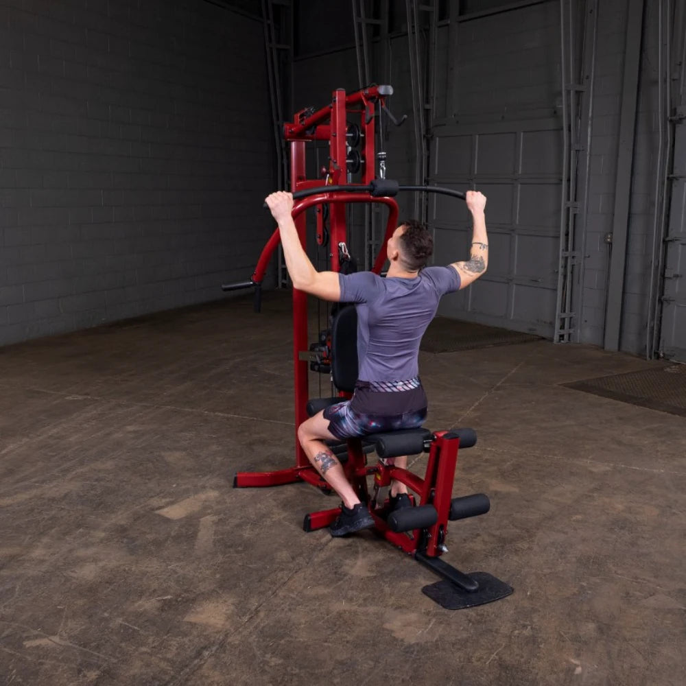 Person performing a lat pull-down exercise on a red gym machine in an industrial-style gym setting.