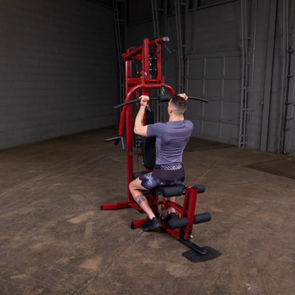 A person using a red multi-gym machine in an industrial-style gym setting, performing an exercise while seated, with a focus on strength training.