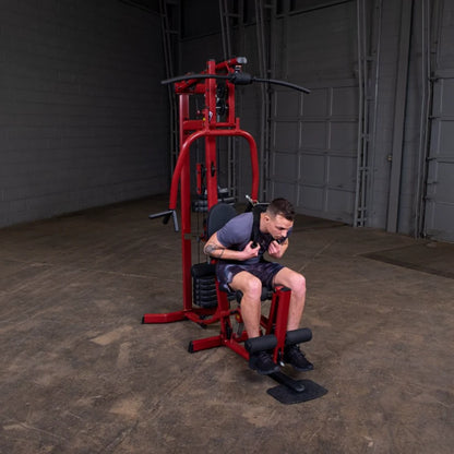 A person using a red multi-gym machine, seated and focused on their workout in a spacious gym environment.