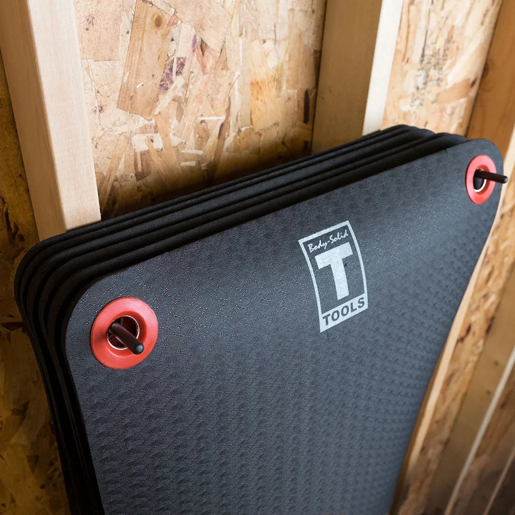 Dark gray foam mat with black binding edges and red carrying handles, featuring a white logo badge on the surface.