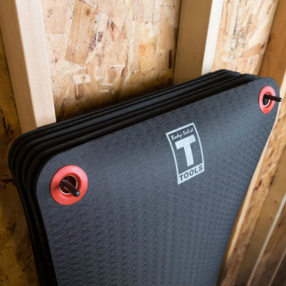 Dark gray foam mat with black binding edges and red carrying handles, featuring a white logo badge on the surface.