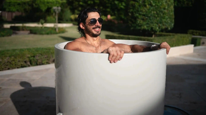 Man relaxing in a white ColdLife cold plunge tub outdoors with sunglasses on