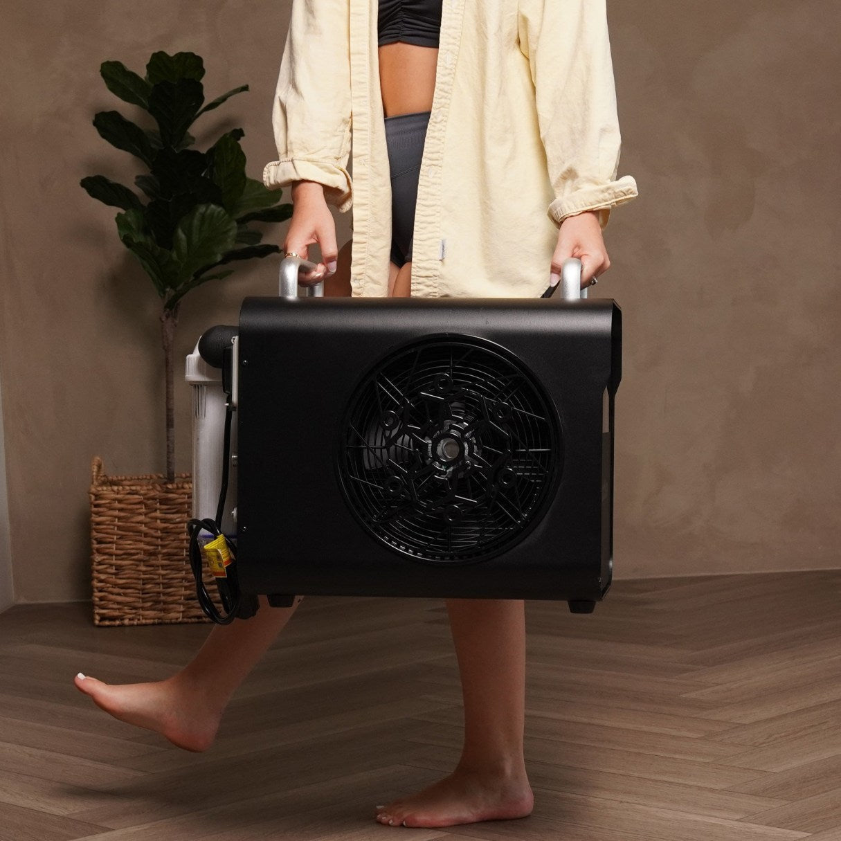 A person carrying the Coldture Water Chiller Pro, featuring a large fan on the side, in a stylish indoor setting.