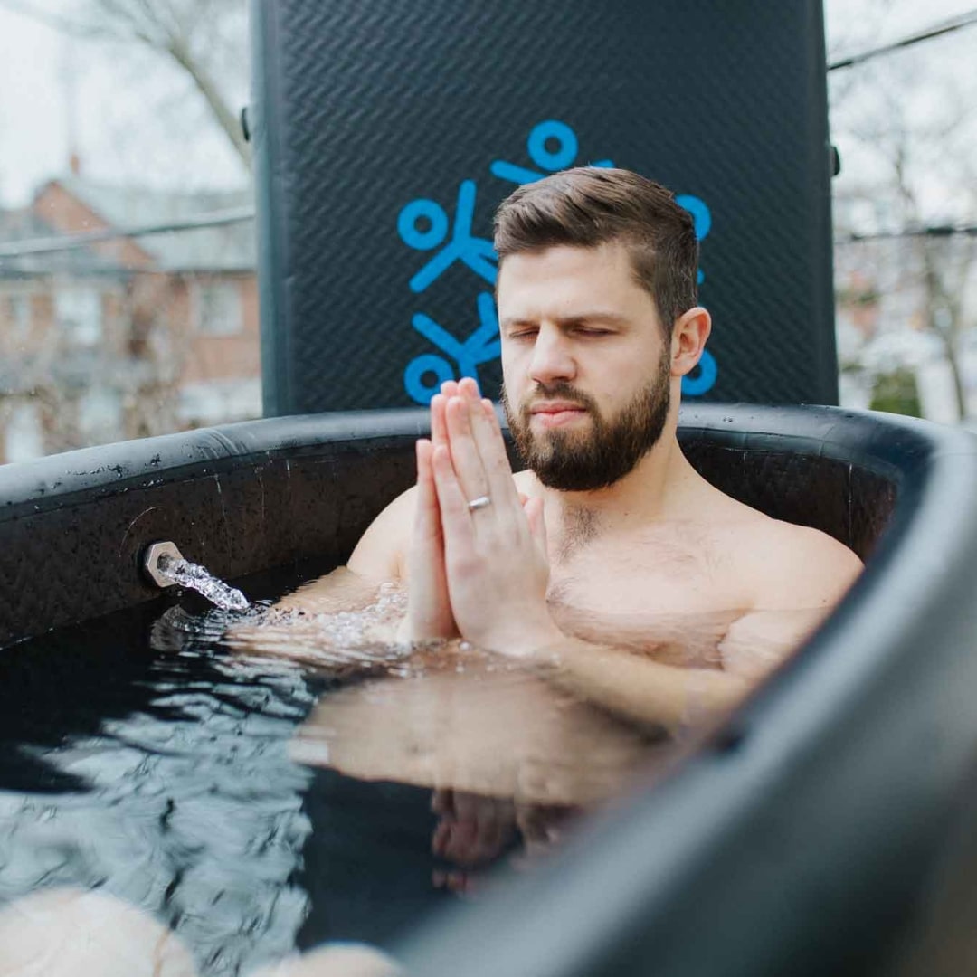 A man sitting in a Coldture Classic + Chiller Pro, with his hands in a prayer position, eyes closed, meditating in a cold water bath.