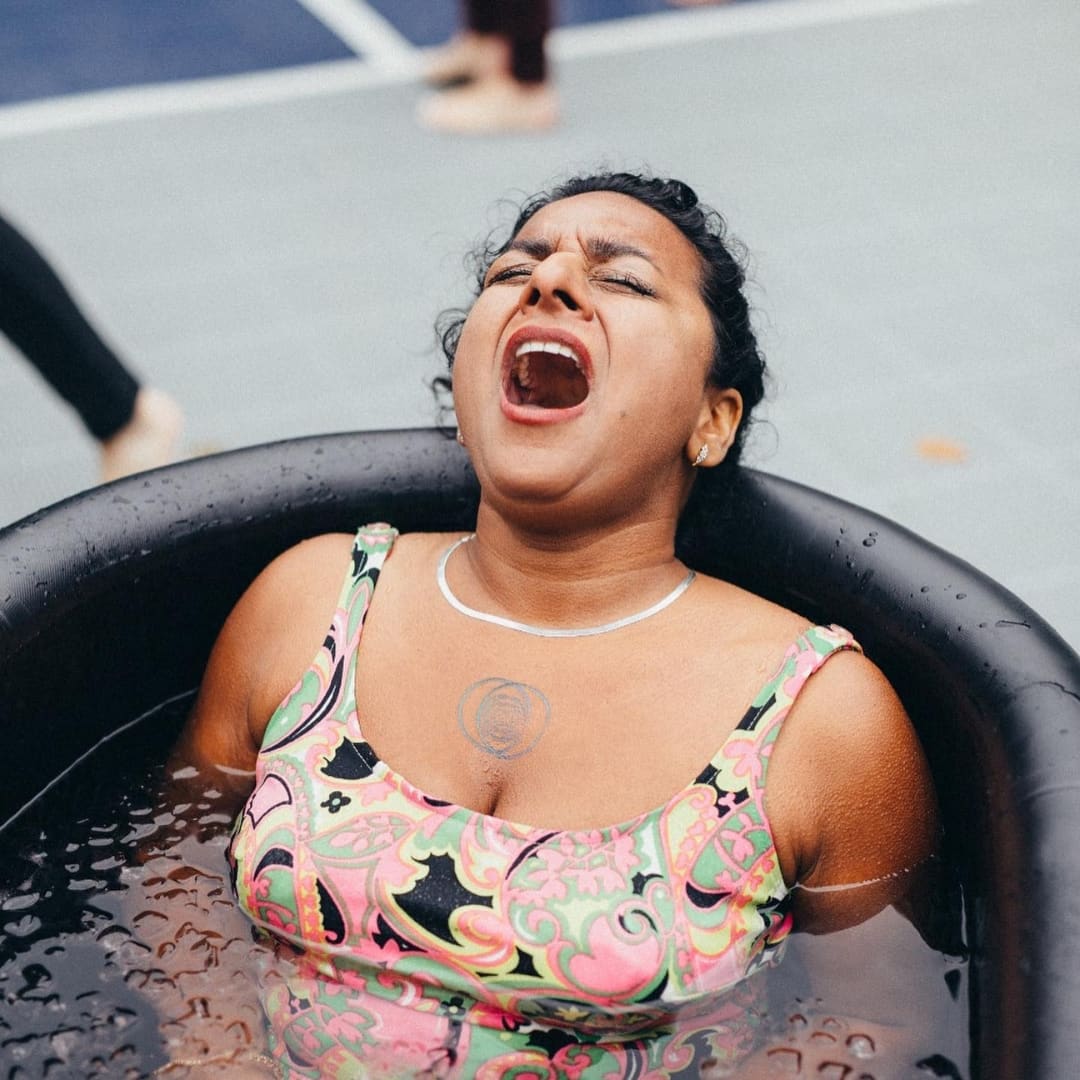 A woman in a colorful swimsuit is submerged in a black tub filled with water, expressing a strong emotion, showcasing the Coldture Classic + Chiller Pro.