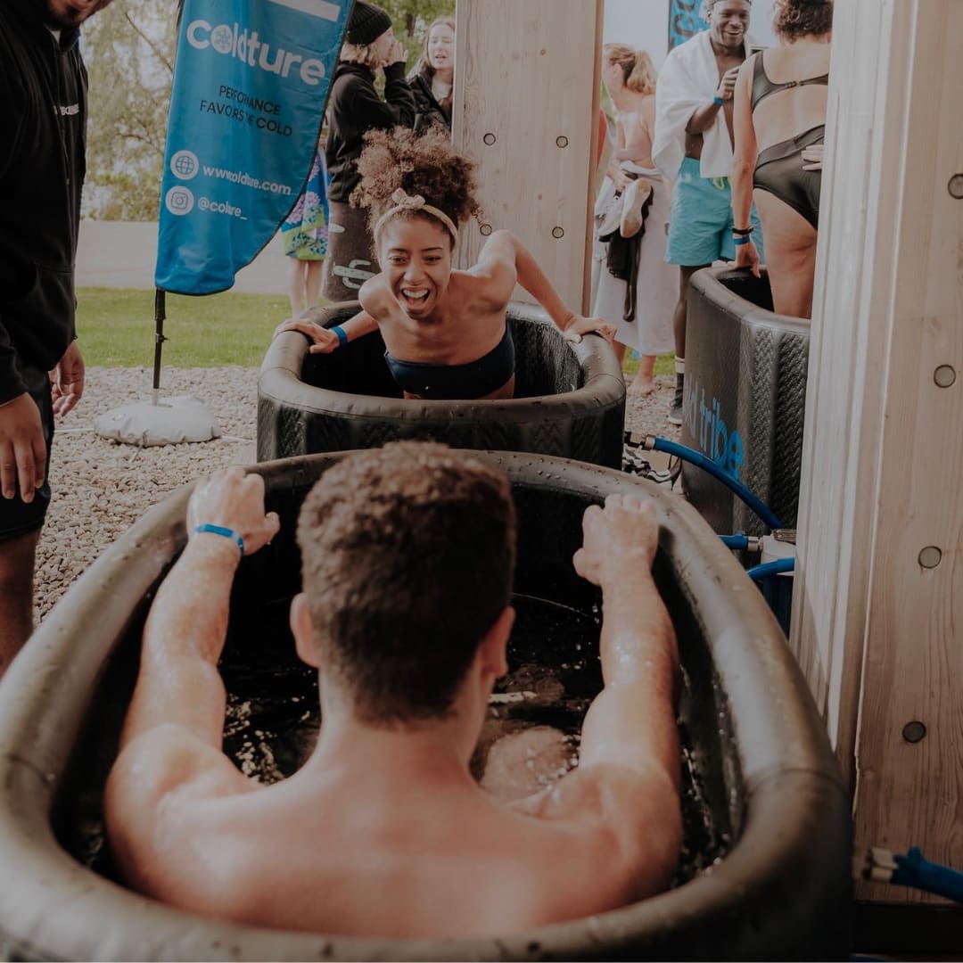 Participants enjoying the Coldture Classic and Chiller Pro ice baths, with one person laughing and reaching towards another in a cold water immersion setup.