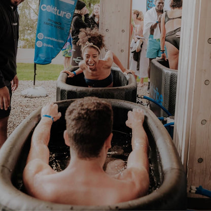 Participants enjoying the Coldture Classic and Chiller Pro ice baths, with one person laughing and reaching towards another in a cold water immersion setup.
