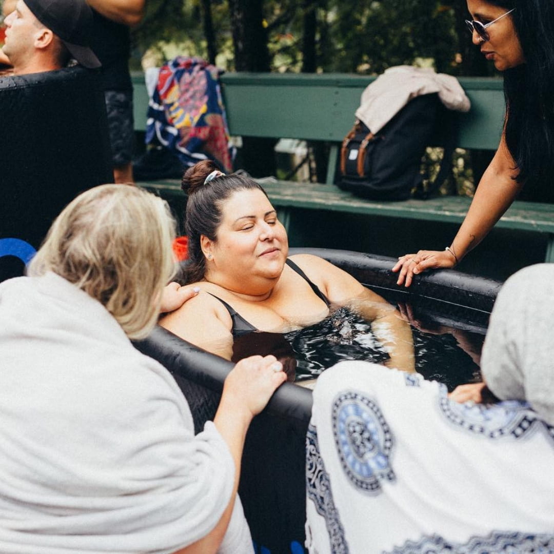 Participants enjoying a group session in a Coldture Classic + Chiller Pro cold plunge, with one woman relaxing in the water while others provide support.