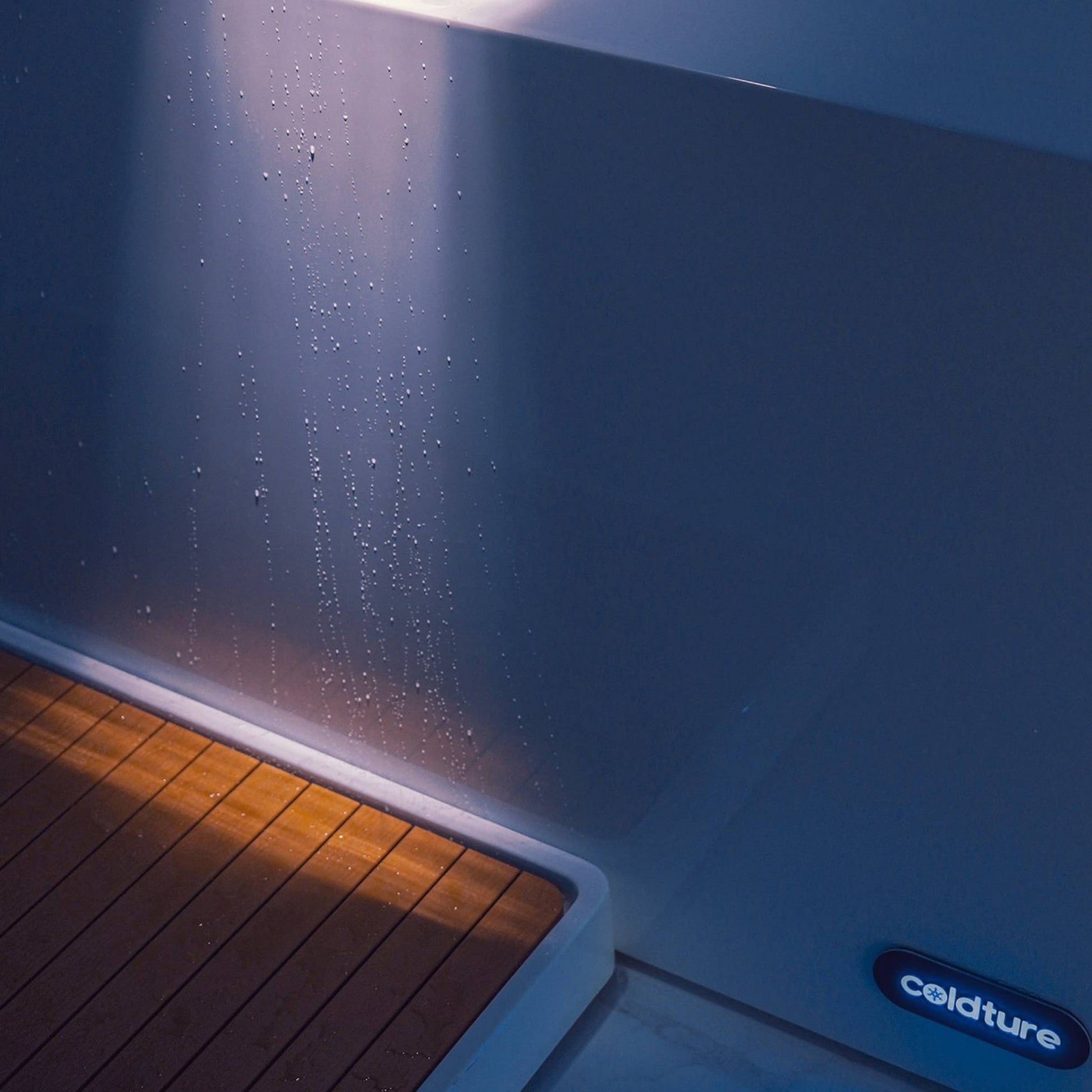 Close-up of the Coldture Pro Plunge with droplets of water on its surface and a wooden deck illuminated by soft light.